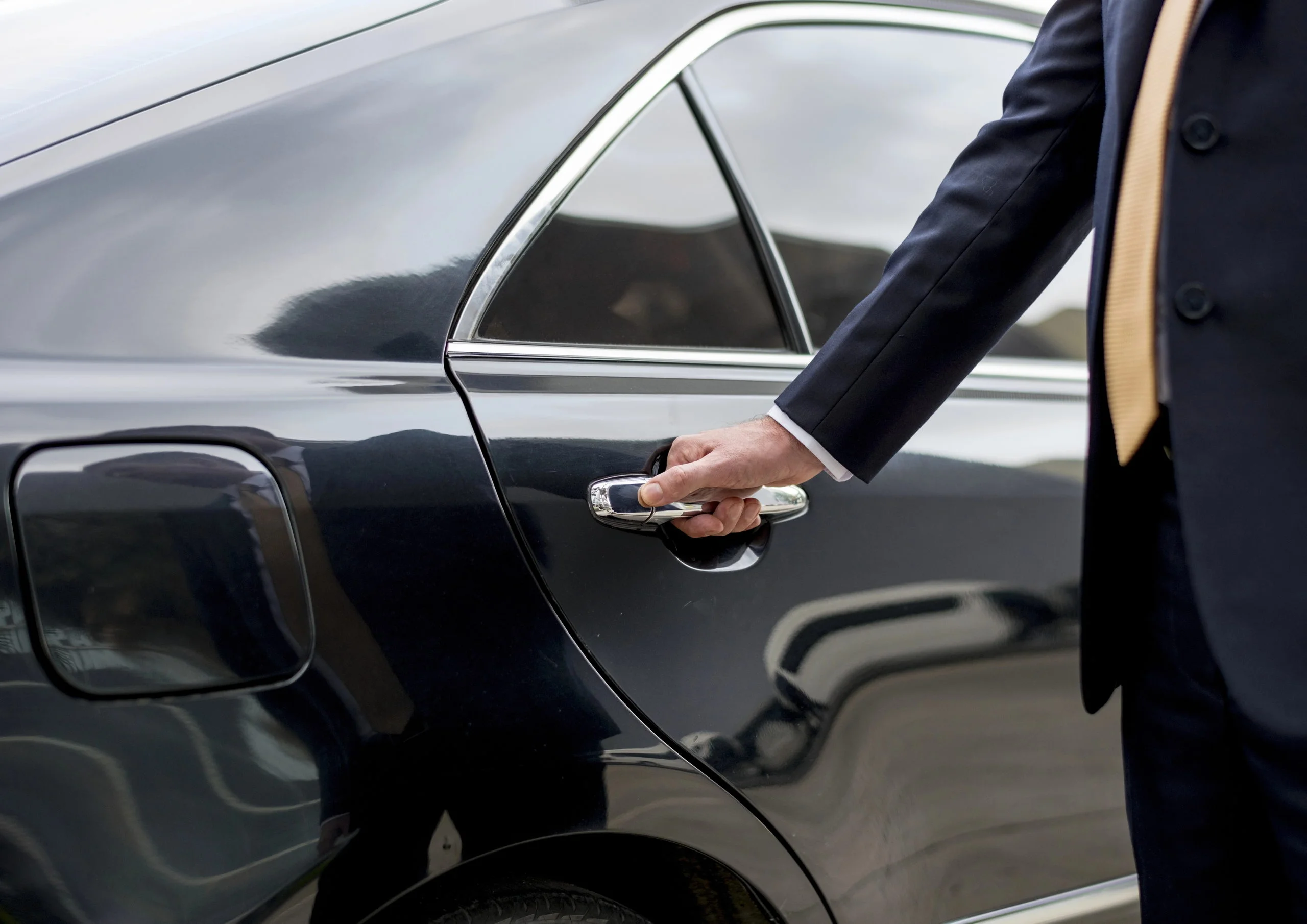 Chauffeur opening the door of a black sedan for a client